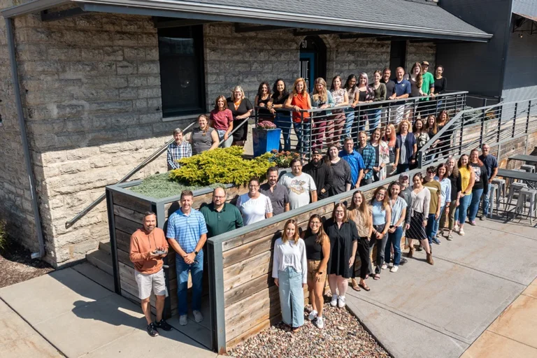 team photo of everyone standing in front of the Blue Door Consulting building